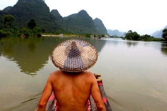 Person looking out over a body of water from a small boat. Greenery and buildings in the background.