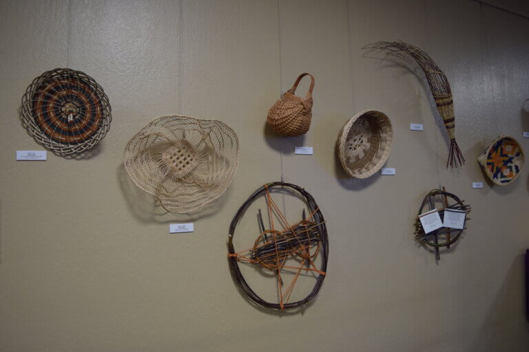 Various woven pieces and baskets on exhibition wall.