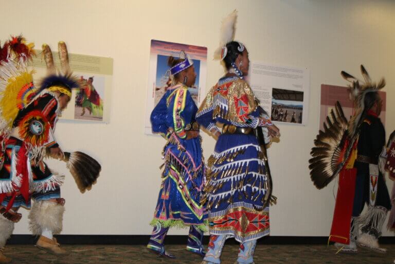 Contemporary Arts and Crafts from the Powwow Tradition exhibition participants dressed in traditional dress in front of the gallery wall.