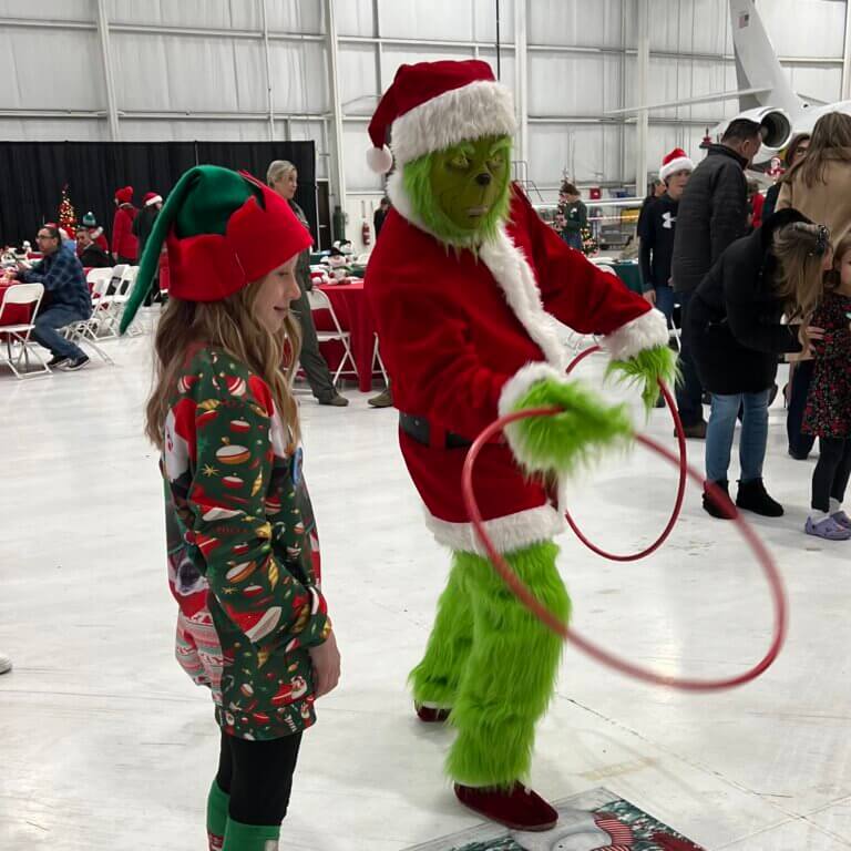 Person dressed as The Grinch playing a ring toss game with little girl