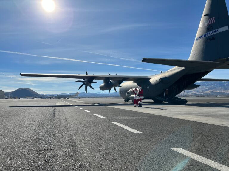 Mr. and Mrs. Claus standing near a C-130 aircraft