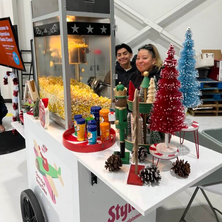 Two people smiling near a popcorn machine