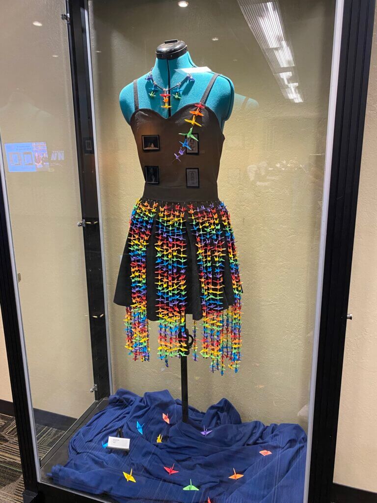 Black dress with colorful paper cranes attached in various ways.